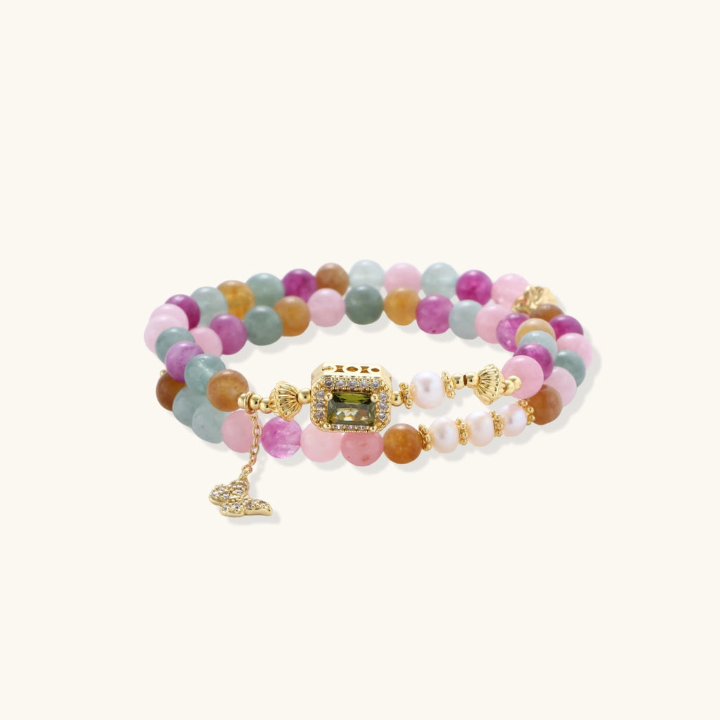 Stretchable bracelet with pastel gemstone beads, freshwater pearls, gold centerpiece and butterfly charm on cream background
